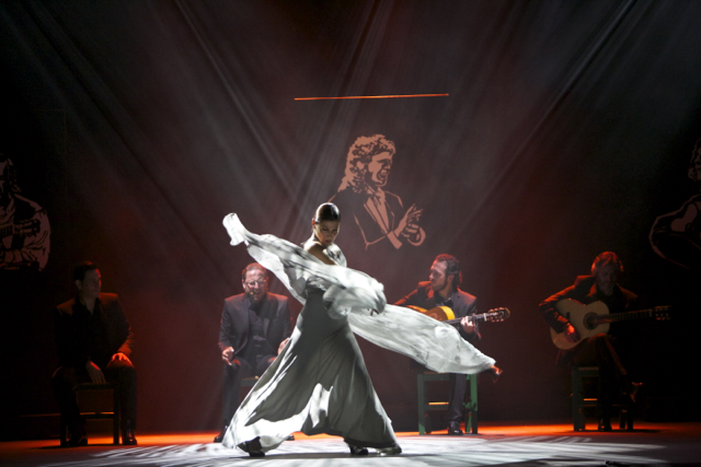 Sara Baras in Voces; Photo: Santana de Yepes. Baras' white scarf cascades around her as she dances flamenco with musicians in the background.